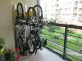 Pionowe przechowywanie roweru na balkonie. Trzy rowery stoją na stojaku, z widokiem na zielony dziedziniec i budynek mieszkalny.