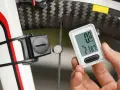 Dłoń trzyma licznik rowerowy pokazujący dystans 21.87 km. Obok widoczny element czujnika na obwodzie koła rowerowego.