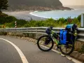 Rower gotowy do bike packingu, obładowany bagażem, stoi przy drodze z widokiem na ocean i plażę.