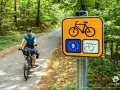 Rowerzysta na leśnej drodze, obok znak szlaku rowerowego krajowego z symbolem UE.