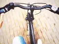Widok z perspektywy rowerzysty. Dłoń trzyma kierownicę, a przed nią widać fragmenty roweru i rozmyte tło. Dowiedz się, jak podnieść kierownicę w rowerze dla lepszego komfortu.