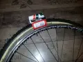 Dwa nowe szytki rowerowe Vittoria Cross XL 33-28" leżą obok czarnej obręczy koła rowerowego.