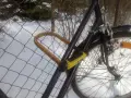Solidne zabezpieczenie roweru przed kradzieżą: gruby, żółty U-lock przypięty do siatki.