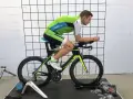 Mężczyzna w stroju kolarskim podczas profesjonalnego fittingu roweru. Czarny rower z zielonymi akcentami stoi na trenażerze.