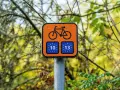 Pomarańczowy znak z rowerem i unijnymi flagami z numerami 10 i 13, wskazujący trasę Euro Velo.