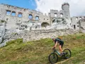 Rowerzysta pokonuje stromy podjazd na tle ruin zamku na Szlaku Orlich Gniazd.
