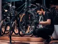 Mechanik w czarnej koszulce i rękawiczkach pokazuje, jak założyć tylne koło w rowerze, pracując w serwisie rowerowym.