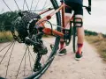Zbliżenie na tylną przerzutkę roweru gravelowego, gdzie widać sprzęgło w przerzutce. Rower stoi na szutrowej drodze, a w tle widać sylwetkę rowerzysty.
