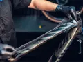 Ręce w czarnych rękawiczkach nakładają folię ochronną na ramę roweru. To kluczowy etap w procesie malowania ram rowerowych, chroniący przed zarysowaniami.