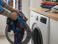 Ręce wkładają kolorową odzież termiczną do otwartej pralki. Dowiedz się, jak prać odzież termiczną, by służyła latami.