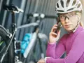 Kobieta w kasku i okularach rowerowych rozmawia przez telefon, obok rower. Dobre okulary na rower to podstawa!