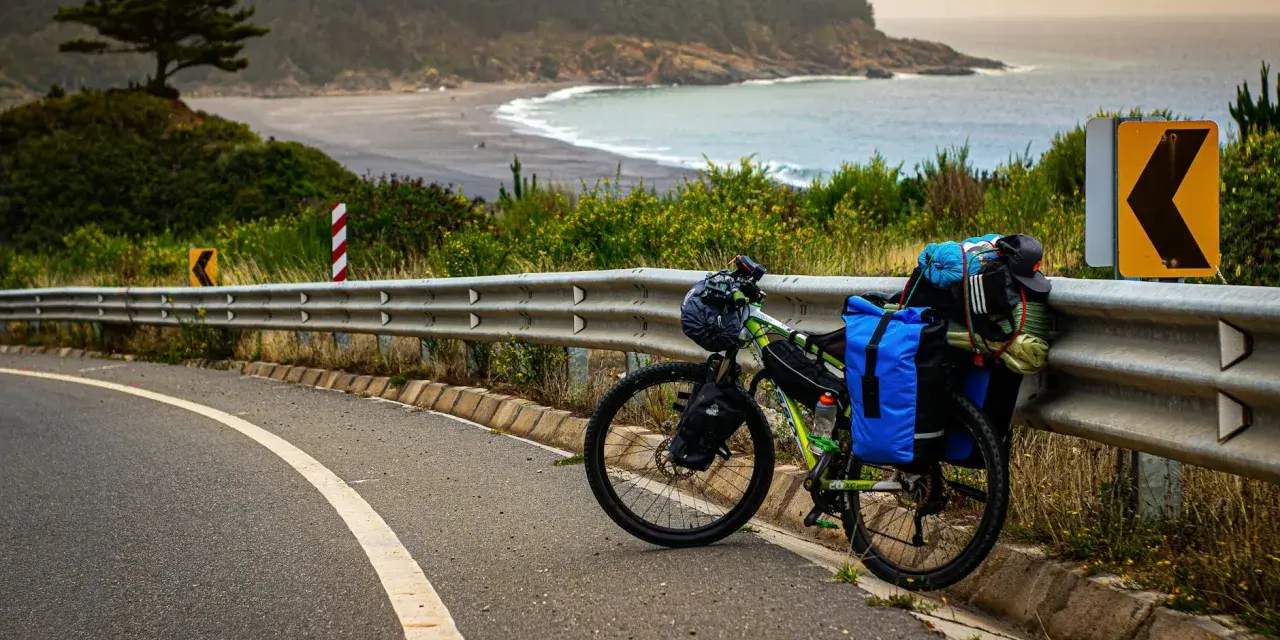 Rower gotowy do bike packingu, obładowany bagażem, stoi przy drodze z widokiem na ocean i plażę.