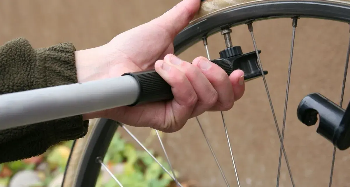 Dłoń trzyma pompkę rowerową, sprawdzając jakie ciśnienie w oponach jest optymalne.