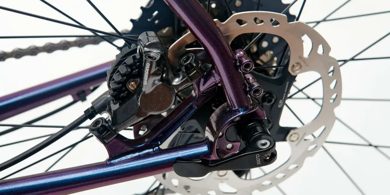 Błyszcząca, fioletowa sztywna oś w rowerze z tarczą hamulcową Shimano i kasetą.