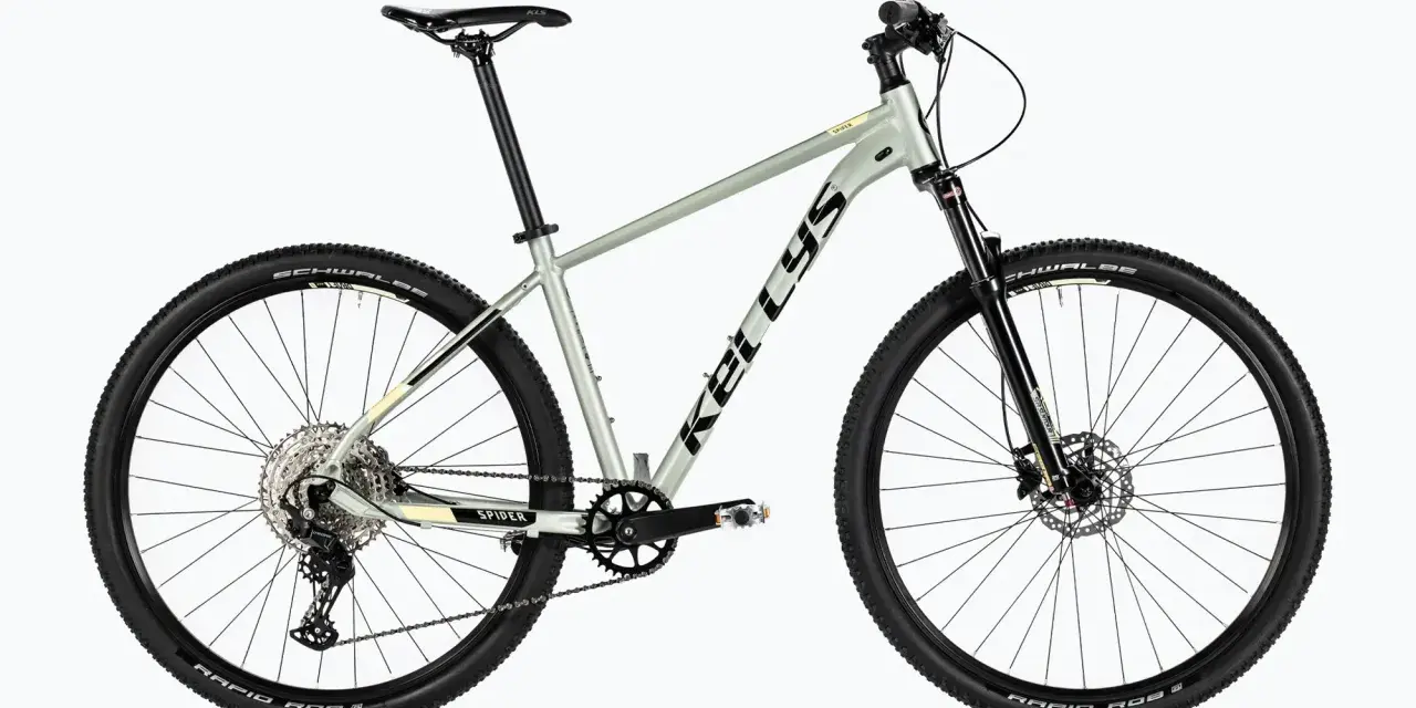 Szary rower Kellys Spider, rower bez amortyzatora, z czarnymi oponami Schwalbe i przerzutkami Shimano.