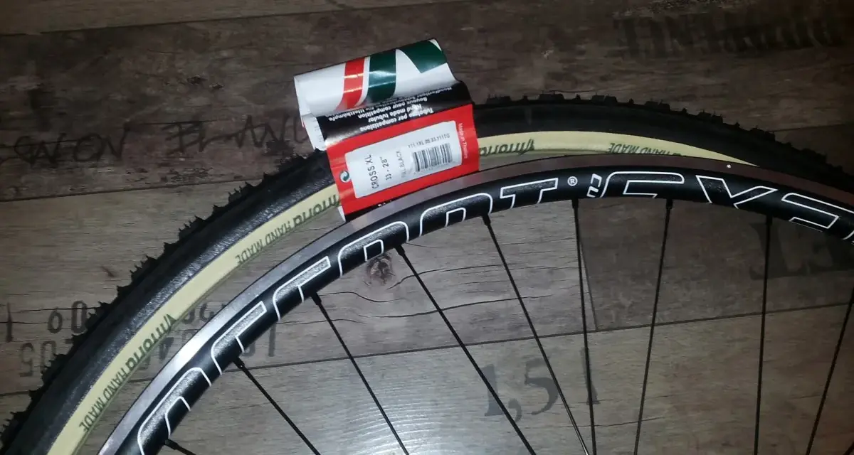 Dwa nowe szytki rowerowe Vittoria Cross XL 33-28" leżą obok czarnej obręczy koła rowerowego.