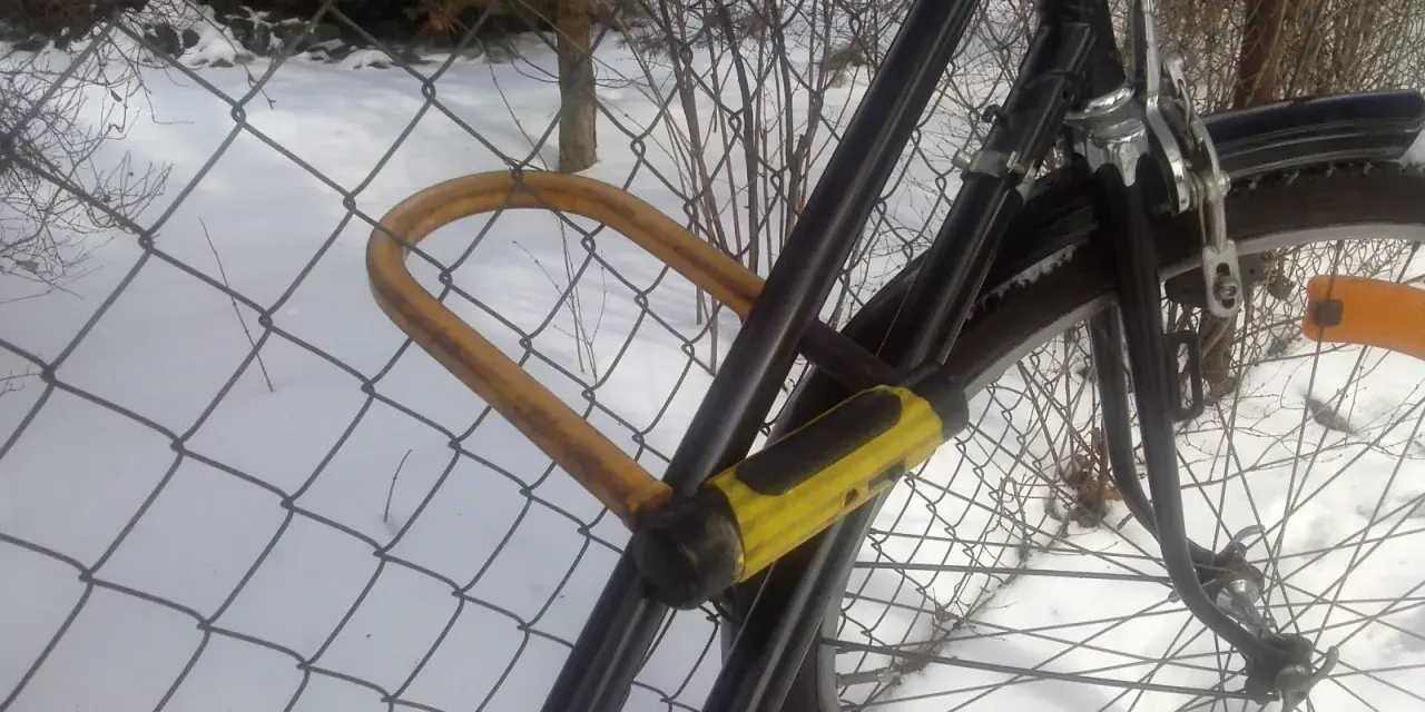 Solidne zabezpieczenie roweru przed kradzieżą: gruby, żółty U-lock przypięty do siatki.