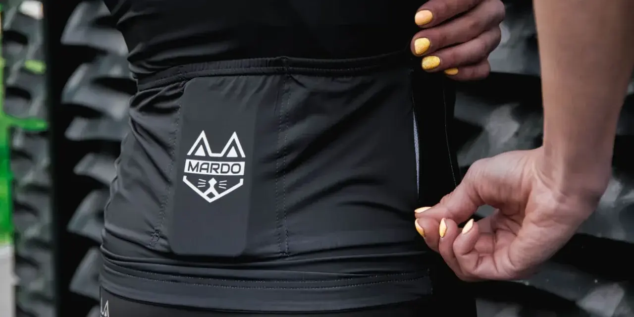 Dłonie z żółtym lakierem zamykają zamek w czarnej odzieży sportowej z logo MARDO. Idealne do prania odzieży sportowej.