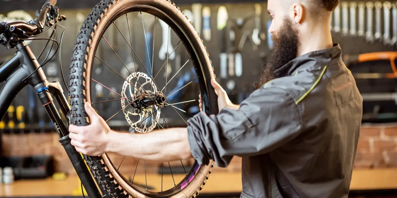 Mechanik z brodą sprawdza oponę gravel. Zastanawia się, ile mleka do opony gravel będzie potrzebne, by zapewnić optymalną jazdę.