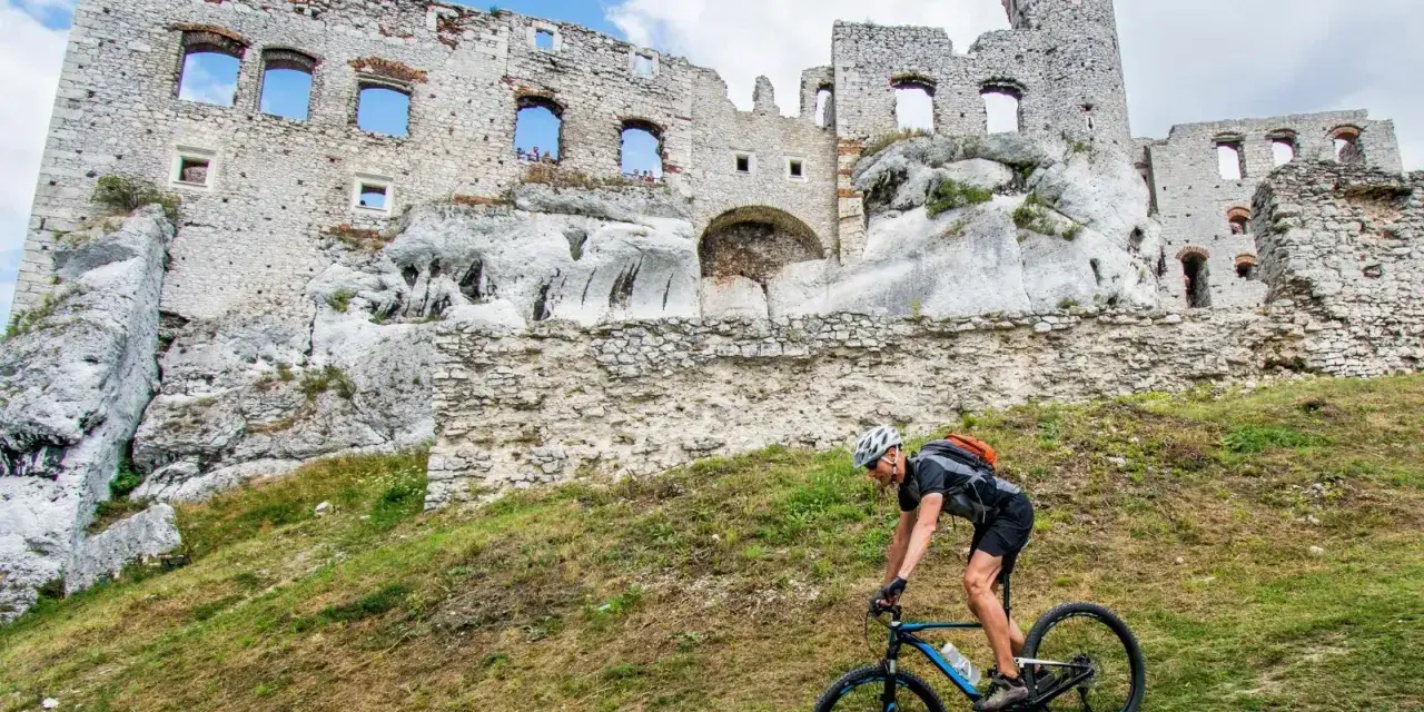 Rowerzysta pokonuje stromy podjazd na tle ruin zamku na Szlaku Orlich Gniazd.