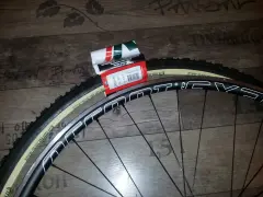 Dwa nowe szytki rowerowe Vittoria Cross XL 33-28" leżą obok czarnej obręczy koła rowerowego.