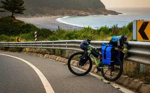 Rower gotowy do bike packingu, obładowany bagażem, stoi przy drodze z widokiem na ocean i plażę.