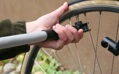 Dłoń trzyma pompkę rowerową, sprawdzając jakie ciśnienie w oponach jest optymalne.