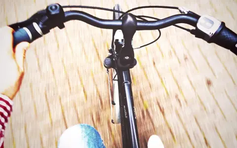 Widok z perspektywy rowerzysty. Dłoń trzyma kierownicę, a przed nią widać fragmenty roweru i rozmyte tło. Dowiedz się, jak podnieść kierownicę w rowerze dla lepszego komfortu.