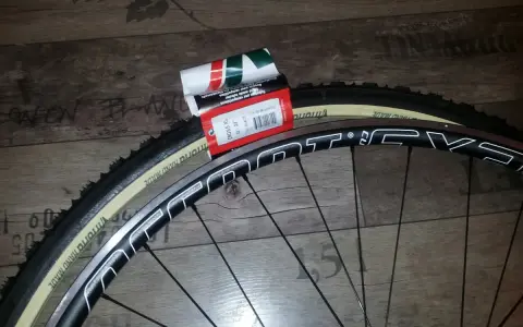 Dwa nowe szytki rowerowe Vittoria Cross XL 33-28" leżą obok czarnej obręczy koła rowerowego.