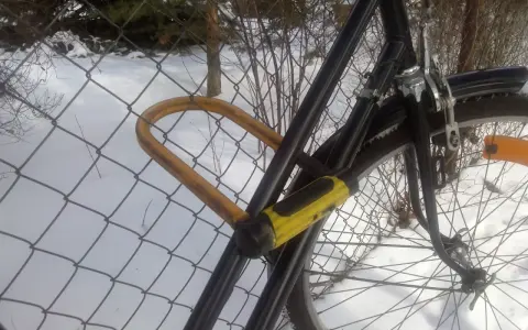 Solidne zabezpieczenie roweru przed kradzieżą: gruby, żółty U-lock przypięty do siatki.