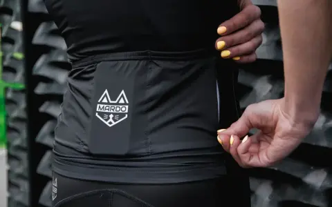 Dłonie z żółtym lakierem zamykają zamek w czarnej odzieży sportowej z logo MARDO. Idealne do prania odzieży sportowej.