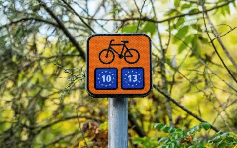 Pomarańczowy znak z rowerem i unijnymi flagami z numerami 10 i 13, wskazujący trasę Euro Velo.