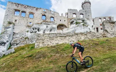 Rowerzysta pokonuje stromy podjazd na tle ruin zamku na Szlaku Orlich Gniazd.