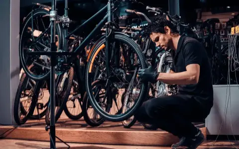 Mechanik w czarnej koszulce i rękawiczkach pokazuje, jak założyć tylne koło w rowerze, pracując w serwisie rowerowym.