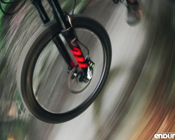 Przednie koło roweru enduro w ruchu, z widocznym amortyzatorem. Różne rodzaje amortyzatorów wpływają na jazdę.