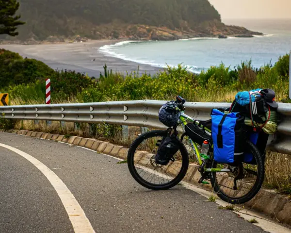 Rower gotowy do bike packingu, obładowany bagażem, stoi przy drodze z widokiem na ocean i plażę.