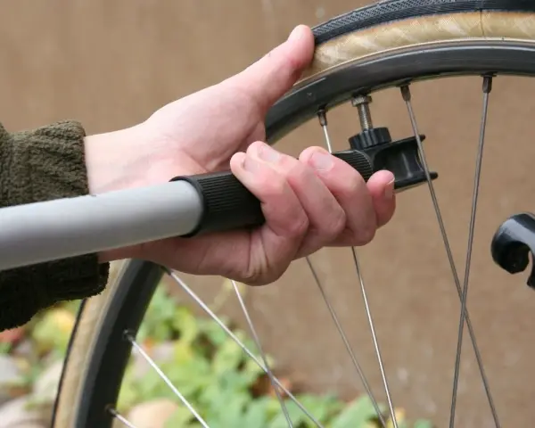 Dłoń trzyma pompkę rowerową, sprawdzając jakie ciśnienie w oponach jest optymalne.