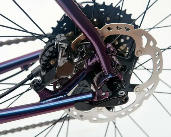 Błyszcząca, fioletowa sztywna oś w rowerze z tarczą hamulcową Shimano i kasetą.