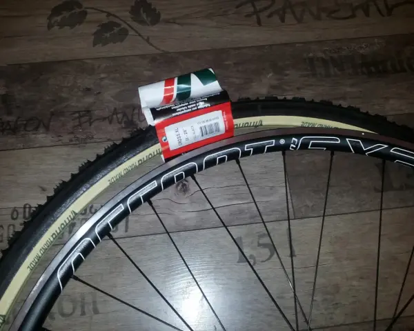 Dwa nowe szytki rowerowe Vittoria Cross XL 33-28" leżą obok czarnej obręczy koła rowerowego.