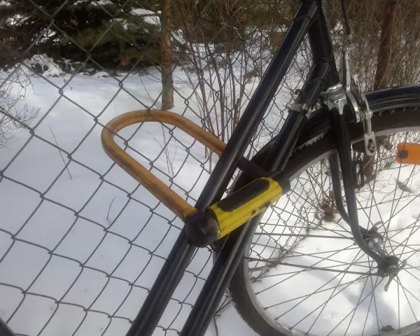 Solidne zabezpieczenie roweru przed kradzieżą: gruby, żółty U-lock przypięty do siatki.