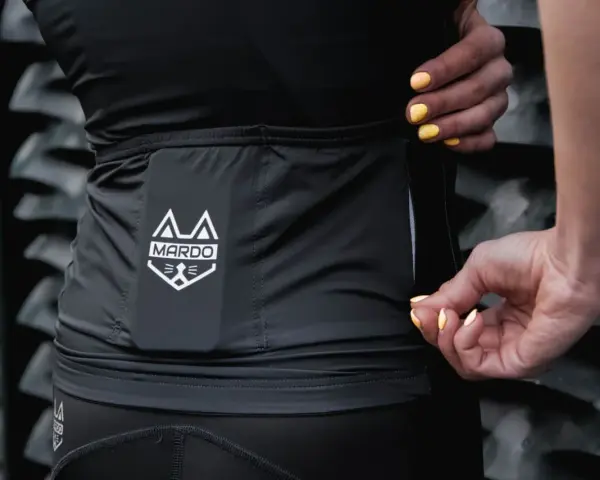 Dłonie z żółtym lakierem zamykają zamek w czarnej odzieży sportowej z logo MARDO. Idealne do prania odzieży sportowej.