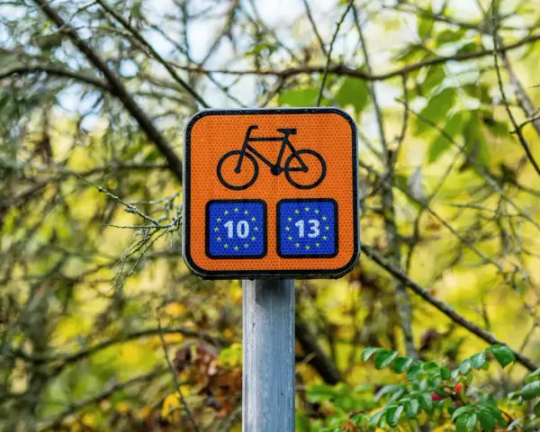 Pomarańczowy znak z rowerem i unijnymi flagami z numerami 10 i 13, wskazujący trasę Euro Velo.