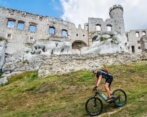 Rowerzysta pokonuje stromy podjazd na tle ruin zamku na Szlaku Orlich Gniazd.