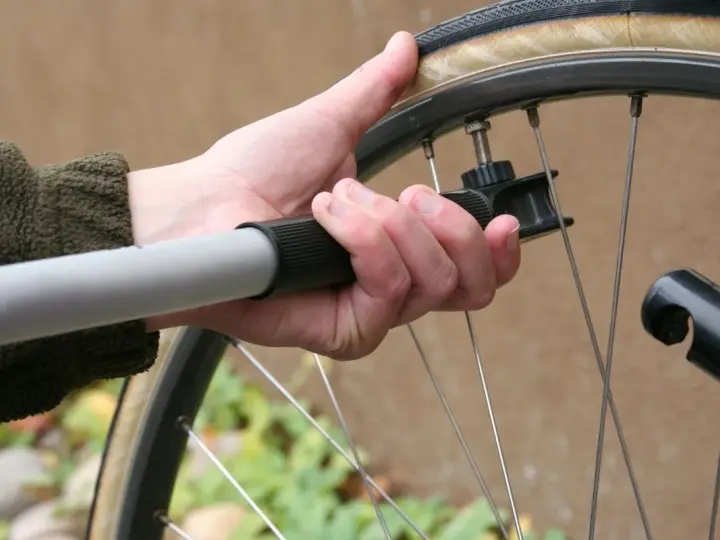 Dłoń trzyma pompkę rowerową, sprawdzając jakie ciśnienie w oponach jest optymalne.