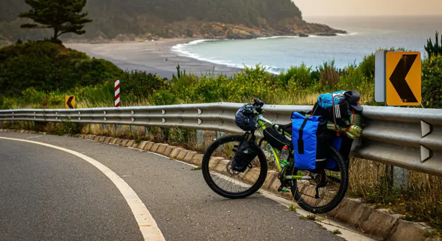 Rower gotowy do bike packingu, obładowany bagażem, stoi przy drodze z widokiem na ocean i plażę.