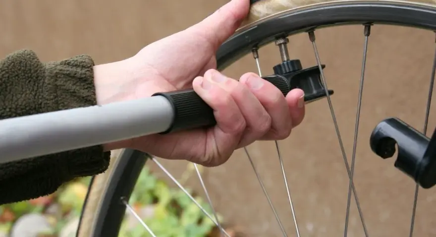 Dłoń trzyma pompkę rowerową, sprawdzając jakie ciśnienie w oponach jest optymalne.