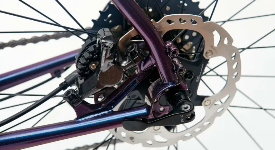 Błyszcząca, fioletowa sztywna oś w rowerze z tarczą hamulcową Shimano i kasetą.