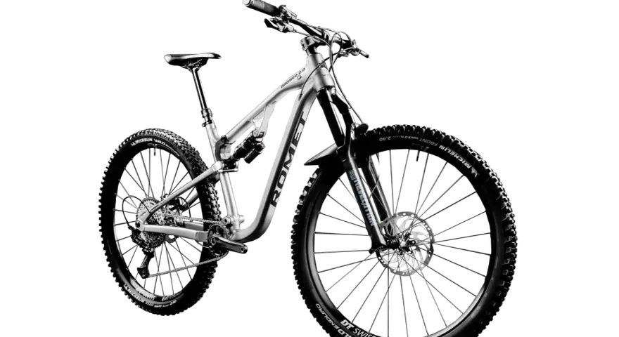 Srebrny rower górski Romet Dagger 2.0 z pełnym zawieszeniem, oponami Michelin Wild Enduro i obręczami DT Swiss M1700. Jedna z wielu marek rowerów.