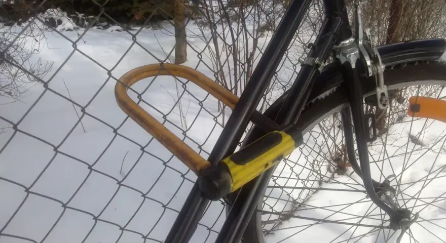 Solidne zabezpieczenie roweru przed kradzieżą: gruby, żółty U-lock przypięty do siatki.