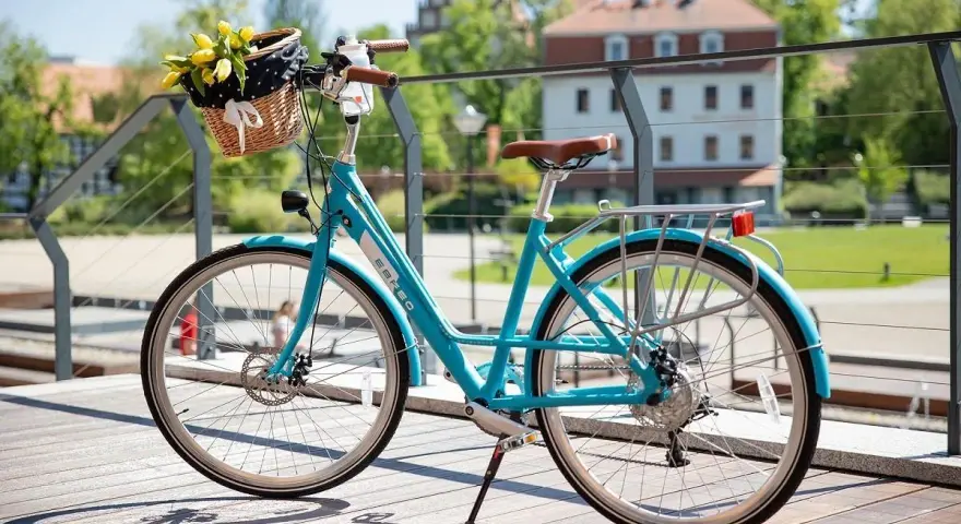 Turkusowy rower z koszykiem pełnym żółtych tulipanów. Dowiedz się, jak zamontować koszyk do roweru, by cieszyć się wiosennymi przejażdżkami.